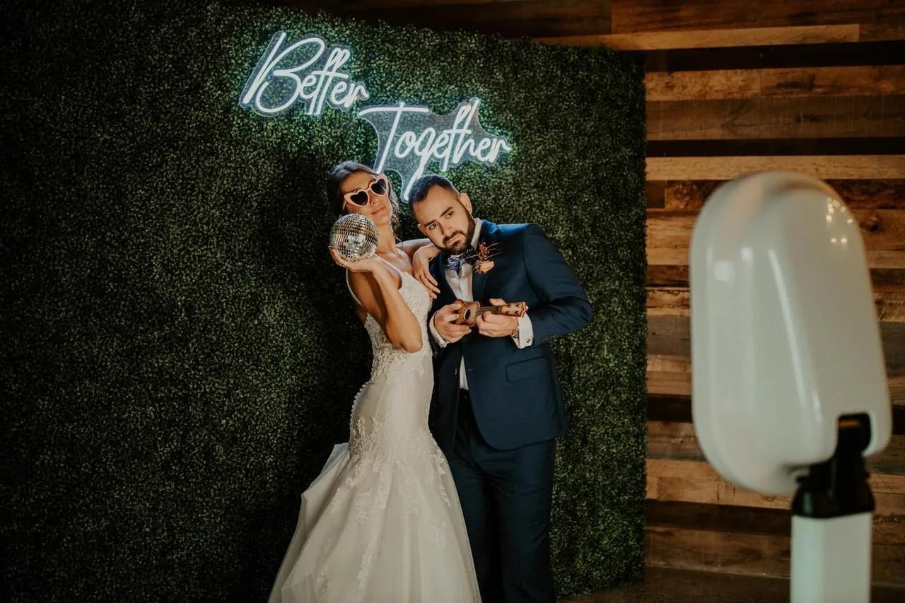 Bride and groom at a photo booth beneath a Better Together neon sign