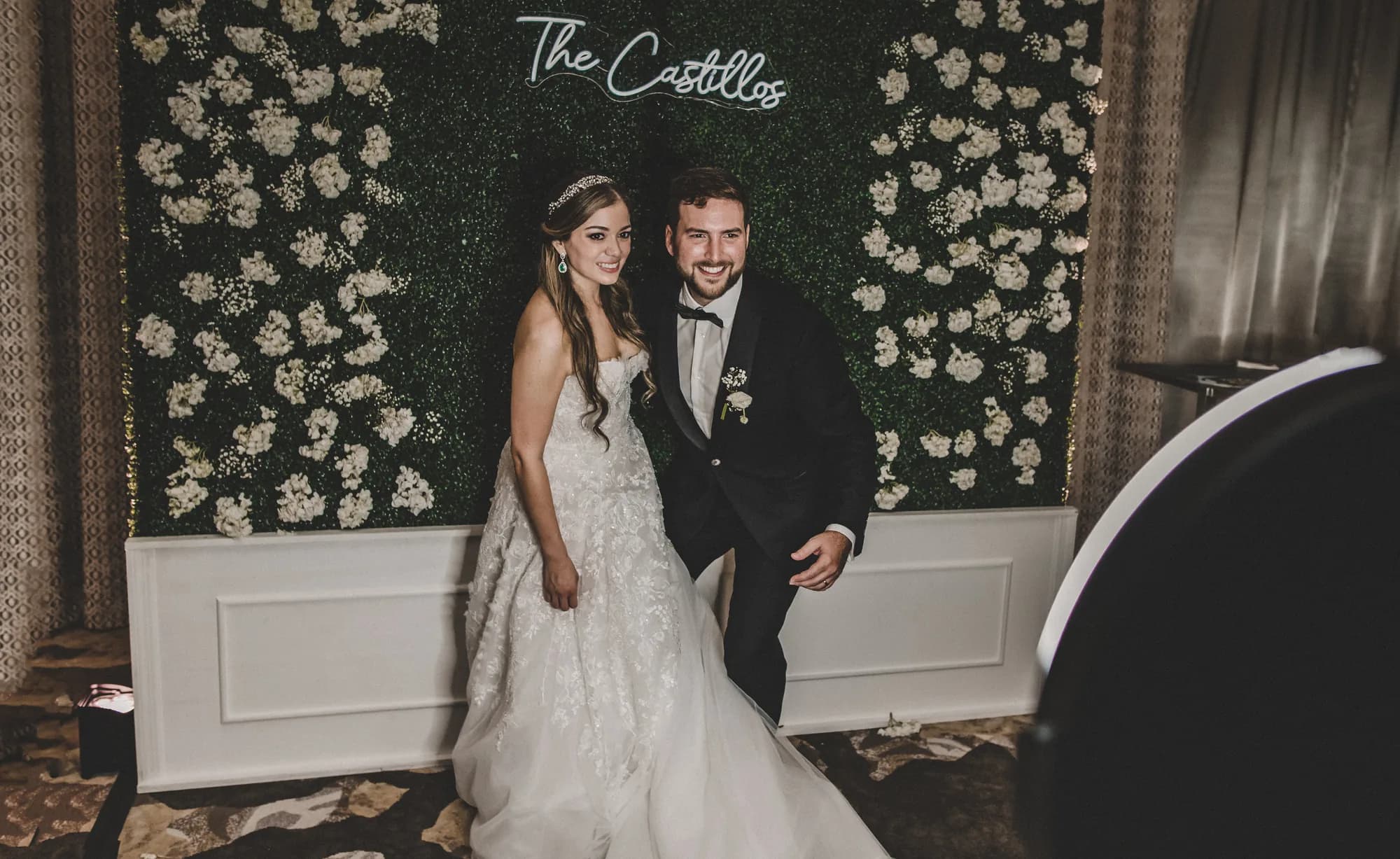 Bride and groom posing at an iRock Your Party photo booth with a white flower wall backdrop in Orlando